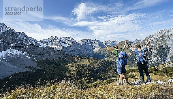 Zwei Bergsteiger Hand in Hand mit ausgestreckten Armen  auf einem Wanderweg  Bergpanorama mit felsigen steilen Gipfeln  Ausblick auf Gipfel Laliderspitze  Dreizinkenspitze und Spritzkarspitze  Wanderung zum Gipfel des Hahnkampl  Engtal  Karwendel  Tirol  Österreich  Europa