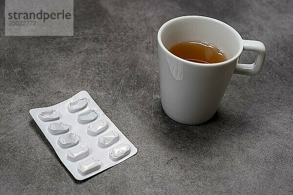 Eine Blisterpackung mit Pillen neben einer Tasse Tee auf grauem Untergrund  Draufsicht  Studioaufnahme  Deutschland  Europa