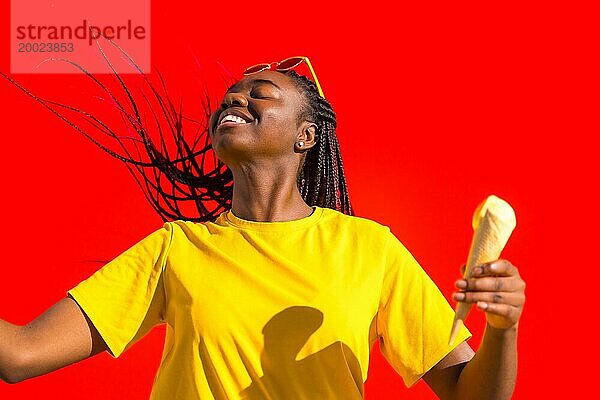 Coole glückliche afrikanische Frau tanzt und isst Eis unter der Sonne und vor einer roten Wand