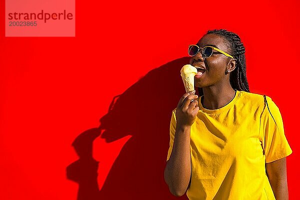 Urbane afrikanische Frau leckt eine Eistüte neben einer roten Wand im Sommer
