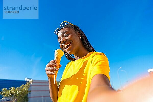 Afrikanische Frau  die ein Selfie macht  während sie an einem sonnigen Tag draußen in der Stadt Eis isst