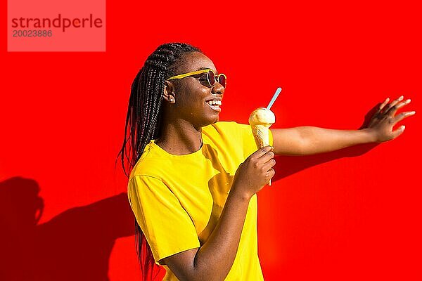 Glückliche junge afrikanische Frau isst ein Eis und lehnt sich an eine rote Wand