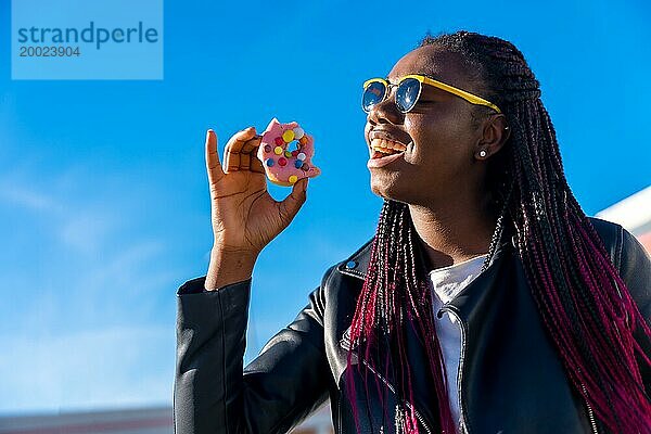 Glückliche afrikanische Frau  die an einem sonnigen Tag im Freien einen Donut isst