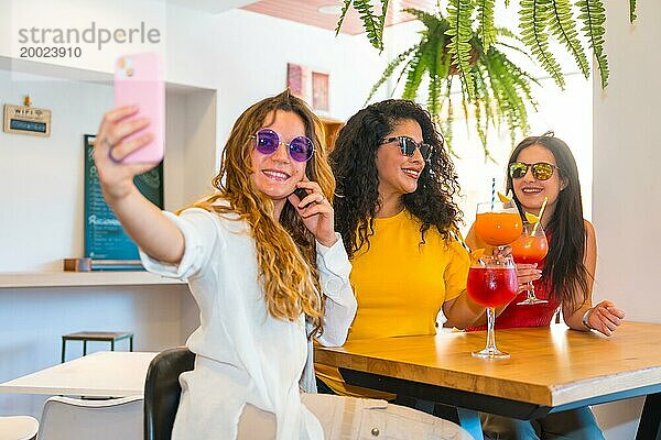 Drei schöne Freundinnen machen ein Selfie  während sie in einer Bar Cocktails trinken