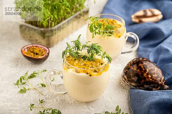 Joghurt mit Passionsfrucht und Ringelblume microgreen im Glas auf grauem Betonhintergrund mit blauem Leinenstoff. Seitenansicht  Nahaufnahme  selektiver Fokus