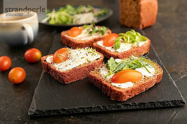 Rote Rüben Brot Sandwiches mit Frischkäse  Tomaten und Mikrogrün auf schwarzem Betonhintergrund. Seitenansicht  Nahaufnahme  selektiver Fokus