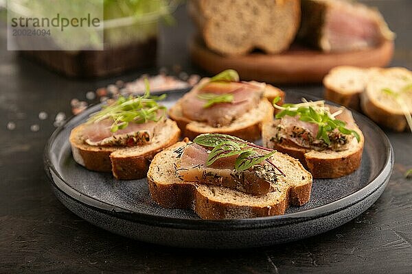 Brotsandwiches mit Jerky Salzfleisch  Sauerampfer und Koriander Mikrogrün auf schwarzem Betonhintergrund. Seitenansicht  Nahaufnahme  selektiver Fokus