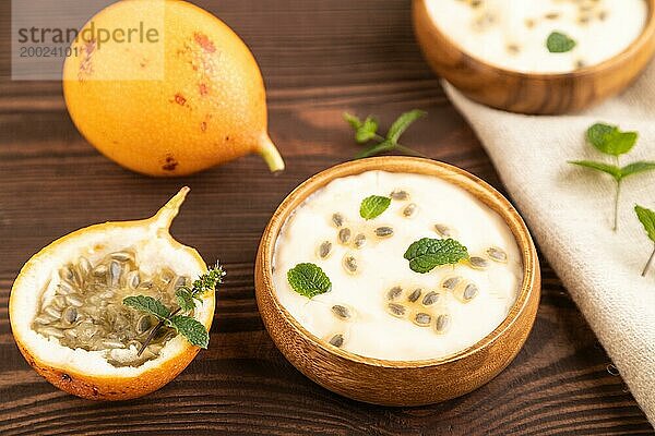 Joghurt mit Granadilla und Minze in Holzschale auf braunem Holzhintergrund und Leinentextil. Seitenansicht  Nahaufnahme  selektiver Fokus