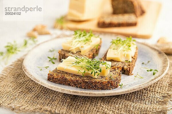 Körnerbrot Sandwiches mit Käse und Brunnenkresse microgreen auf grauem Beton Hintergrund und Leinen Textil. Seitenansicht  Nahaufnahme  selektiver Fokus