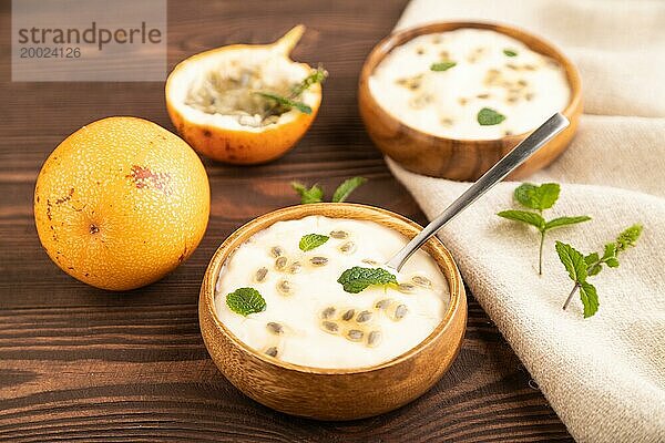 Joghurt mit Granadilla und Minze in Holzschale auf braunem Holzhintergrund und Leinentextil. Seitenansicht  Nahaufnahme  selektiver Fokus