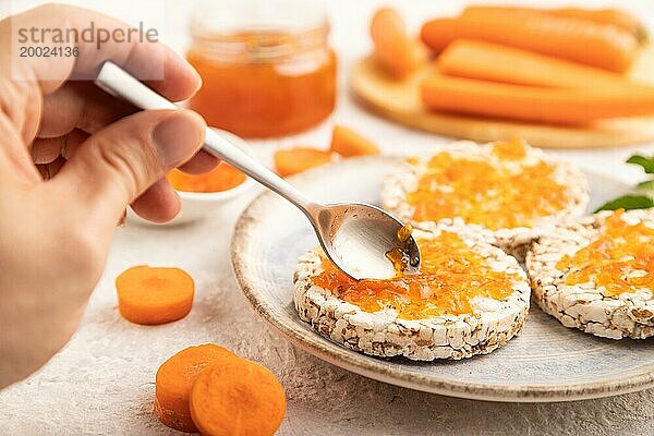 Karottenmarmelade mit Puffreiskuchen auf grauem Betonhintergrund mit Hand. Seitenansicht  Nahaufnahme  selektiver Fokus