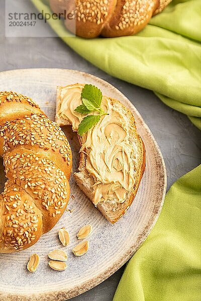 Hausgemachtes süßes Brötchen mit Erdnussbutter und Tasse Kaffee auf grauem Betonhintergrund und grünem Leinenstoff. Seitenansicht  Nahaufnahme  selektiver Fokus