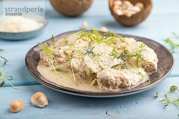 Geschmorte Hühnerfilets mit Kokosmilchsauce und Mizunakraut Mikrogrün auf blauem Holzhintergrund. Seitenansicht  Nahaufnahme  selektiver Fokus