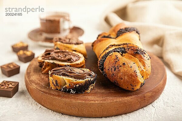 Hausgemachtes süßes Brötchen mit Schokoladencreme und Tasse Kaffee auf grauem Betonhintergrund und Leinenstoff. Seitenansicht  Nahaufnahme  selektiver Fokus