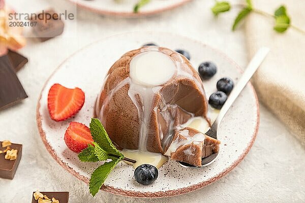 Schokoladengelee mit Erdbeere  Heidelbeere und Milchcreme mit Löffel auf grauem Betonhintergrund und Leinenstoff geschnitten. Seitenansicht  Nahaufnahme  selektiver Fokus