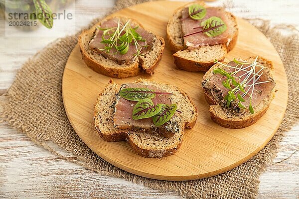 Brotsandwiches mit gesalzenem Dörrfleisch  Sauerampfer und Koriander Mikrogrün auf weißem Holzhintergrund und Leinenstoff. Seitenansicht  Nahaufnahme  selektiver Fokus