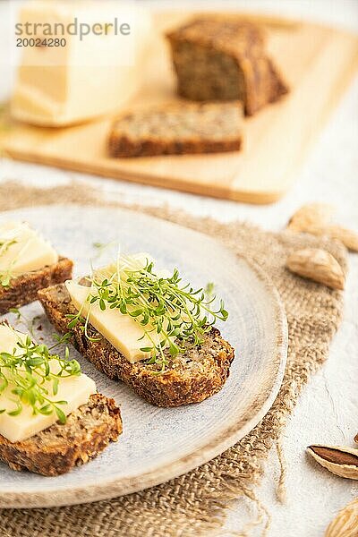 Körnerbrot Sandwiches mit Käse und Brunnenkresse microgreen auf grauem Beton Hintergrund und Leinen Textil. Seitenansicht  Nahaufnahme  selektiver Fokus