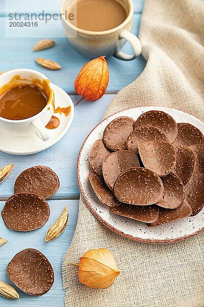 Schokoladenchips mit einer Tasse Kaffee und Karamell auf einem blauen Holzhintergrund und Leinenstoff. Seitenansicht  Nahaufnahme  selektiver Fokus