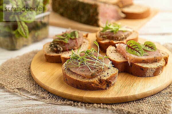 Brotsandwiches mit gesalzenem Dörrfleisch  Sauerampfer und Koriander Mikrogrün auf weißem Holzhintergrund und Leinenstoff. Seitenansicht  Nahaufnahme  selektiver Fokus