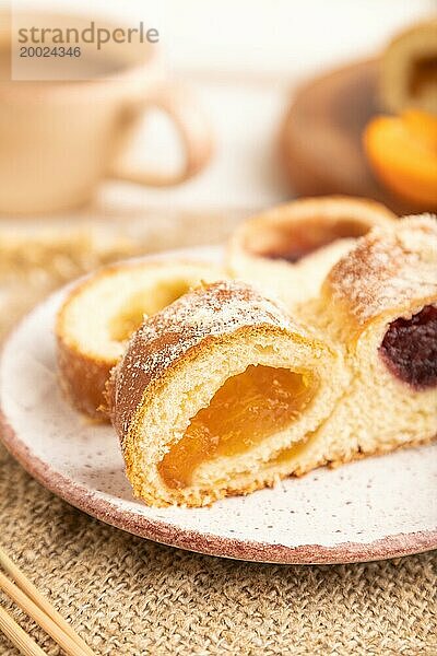 Hausgemachtes süßes Brötchen mit Aprikosenmarmelade und Tasse Kaffee auf weißem Holzhintergrund und Leinenstoff. Seitenansicht  Nahaufnahme  selektiver Fokus