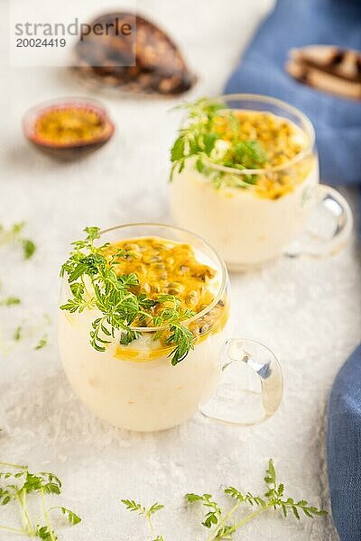 Joghurt mit Passionsfrucht und Ringelblume microgreen im Glas auf grauem Betonhintergrund mit blauem Leinenstoff. Seitenansicht  Nahaufnahme  selektiver Fokus