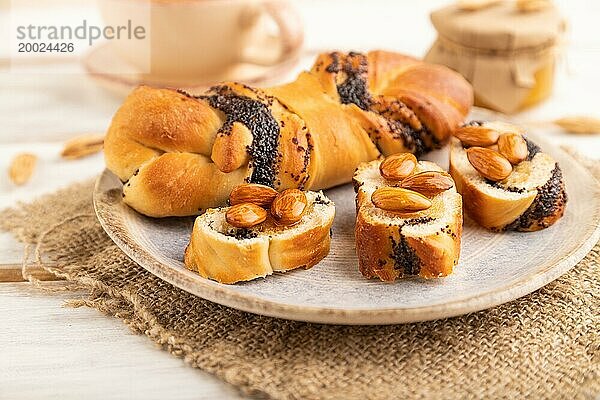 Hausgemachtes süßes Brötchen mit Honigmandeln und einer Tasse grünem Tee auf einem weißen hölzernen Hintergrund und Leinenstoff. Seitenansicht  Nahaufnahme  selektiver Fokus