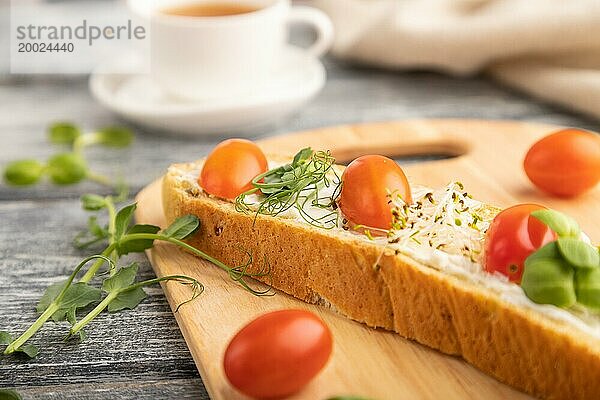 Langes Weißbrot Sandwich mit Frischkäse  Tomaten und Mikrogrün auf grauem Holzhintergrund und Leinenstoff. Seitenansicht  Nahaufnahme  selektiver Fokus