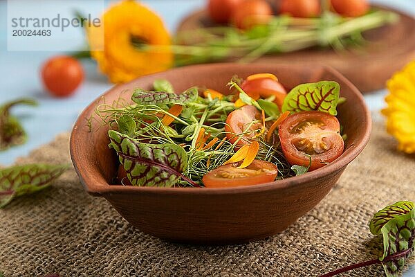 Vegetarischer Gemüsesalat aus Tomaten  Ringelblumenblüten  mikrogrünen Sprossen auf blauem Holzhintergrund und Leinentuch. Seitenansicht  Nahaufnahme  selektiver Fokus