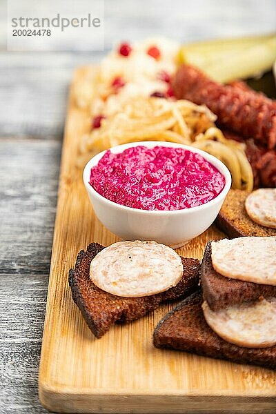 Snacks: Würstchen  Toast  Sauerkraut  marinierte Zwiebeln und Gurken  gebackene Kartoffeln auf einem Schneidebrett auf einem grauen Holzhintergrund. Seitenansicht  Nahaufnahme  selektiver Fokus