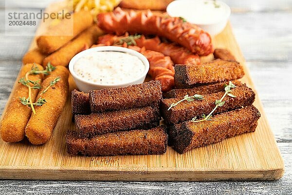 Verschiedene Snacks: Würstchen  Nuggets  Käsestangen  Toast  Krautsalat auf einem Schneidebrett auf einem grauen Holzhintergrund. Seitenansicht  Nahaufnahme  selektiver Fokus