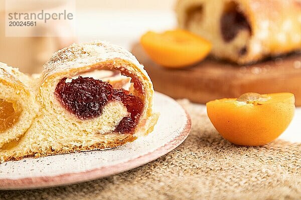 Hausgemachtes süßes Brötchen mit Aprikosenmarmelade und Tasse Kaffee auf weißem Holzhintergrund und Leinenstoff. Seitenansicht  Nahaufnahme  selektiver Fokus