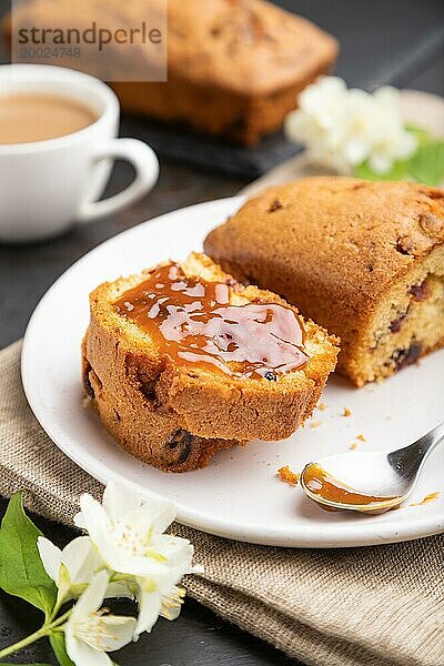 Hausgemachter Kuchen mit Rosinen  Mandeln  weichem Karamell und einer Tasse Kaffee auf einem schwarzen Betonhintergrund und Leinenstoff. Seitenansicht  Nahaufnahme  selektiver Fokus