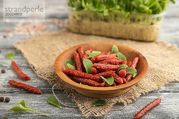 Kleine geräucherte Wurst mit Borretsch Mikrogrün  Salz und Pfeffer auf grauem Holzhintergrund und Leinenstoff. Seitenansicht  Nahaufnahme  selektiver Fokus