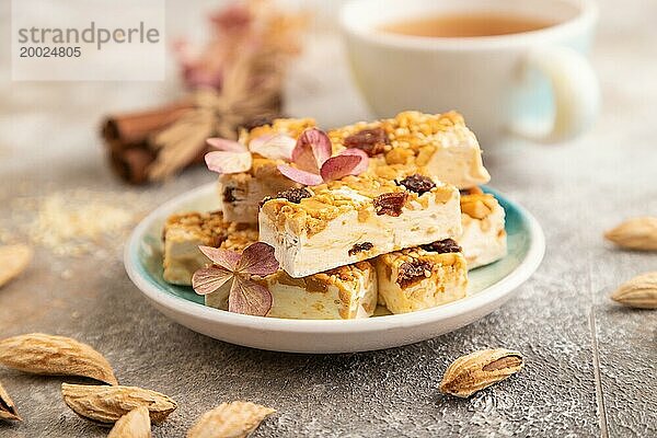 Traditionelle Süßigkeiten Nougat mit Nüssen und Sesam mit Tasse grünem Tee auf braunem Beton Hintergrund. Seitenansicht  Nahaufnahme  selektiver Fokus