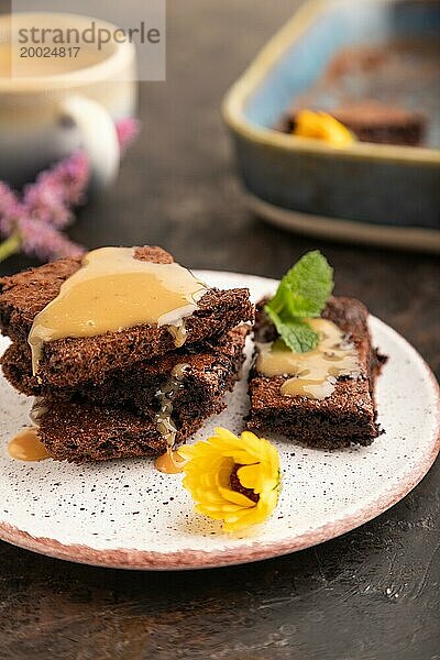 Schokolade Brownie mit Karamell Sauce mit einer Tasse Kaffee auf schwarzem Beton Hintergrund. Seitenansicht  Nahaufnahme  selektiver Fokus