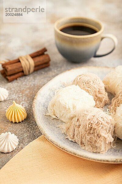 Traditionelle arabische Süßigkeiten Pishmanie und eine Tasse Kaffee auf braunem Betonhintergrund und orangefarbenem Leinenstoff. Seitenansicht  Nahaufnahme  selektiver Fokus