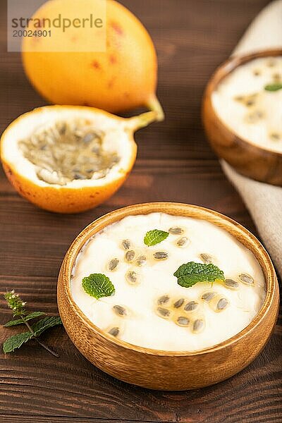 Joghurt mit Granadilla und Minze in Holzschale auf braunem Holzhintergrund und Leinentextil. Seitenansicht  Nahaufnahme  selektiver Fokus