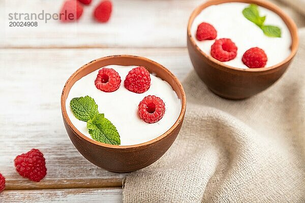 Joghurt mit Himbeeren in Tonbechern auf weißem Holzhintergrund und Leinentuch. Seitenansicht  Nahaufnahme  selektiver Fokus