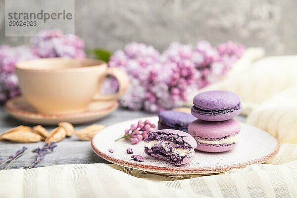 Lila Macarons oder Makronen Kuchen mit Tasse Kaffee auf einem grauen hölzernen Hintergrund und weißem Leinen Textil. Seitenansicht  Nahaufnahme  selektiver Fokus