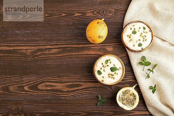Joghurt mit Granadilla und Minze in Holzschüssel auf braunem Holzhintergrund und Leinentextil. Draufsicht  flat lay  copy space