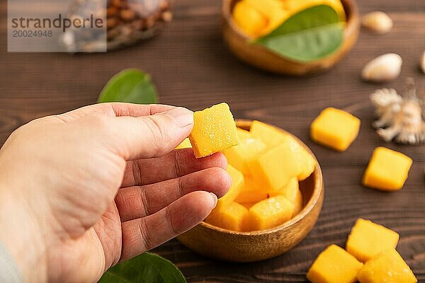 Getrocknete und kandierte Mangowürfel in Holzschalen auf braunem  hölzernem  strukturiertem Hintergrund mit Hand. Seitenansicht  Nahaufnahme  selektiver Fokus  veganes  vegetarisches Lebensmittelkonzept