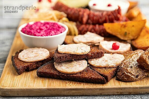 Snacks: Würstchen  Toast  Sauerkraut  marinierte Zwiebeln und Gurken  gebackene Kartoffeln auf einem Schneidebrett auf einem grauen Holzhintergrund. Seitenansicht  Nahaufnahme  selektiver Fokus