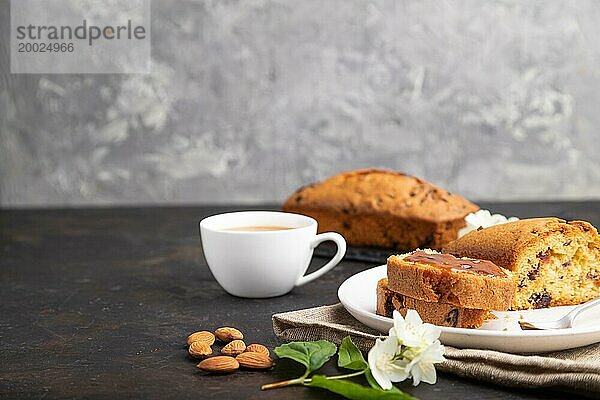 Hausgemachter Kuchen mit Rosinen  Mandeln  weichem Karamell und einer Tasse Kaffee auf schwarzem Betonhintergrund und Leinenstoff. Seitenansicht  Kopierraum  selektiver Fokus