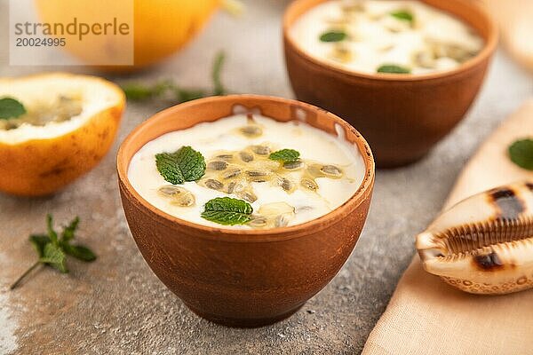 Joghurt mit Granadilla und Minze in Tonschale auf braunem Betonhintergrund und orangefarbenem Leinentextil. Seitenansicht  Nahaufnahme  selektiver Fokus