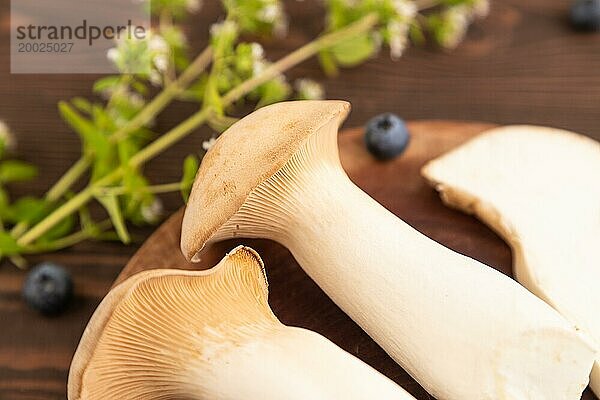 Braune Kräuter Seitlinge (Pleurotus eryngii) auf braunem Holzhintergrund mit Heidelbeeren  Kräutern und Gewürzen. Seitenansicht  selektiver Fokus