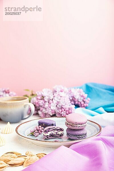 Lila Makronen oder Makronen Kuchen mit Tasse Kaffee auf einem weißen und rosa Hintergrund und magenta blauen Textil. Seitenansicht  Kopierraum  selektiver Fokus