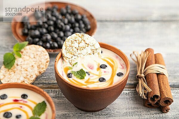 Joghurt mit Heidelbeeren und Karamell in Tonschale auf grauem Holzhintergrund. Seitenansicht  Nahaufnahme  selektiver Fokus