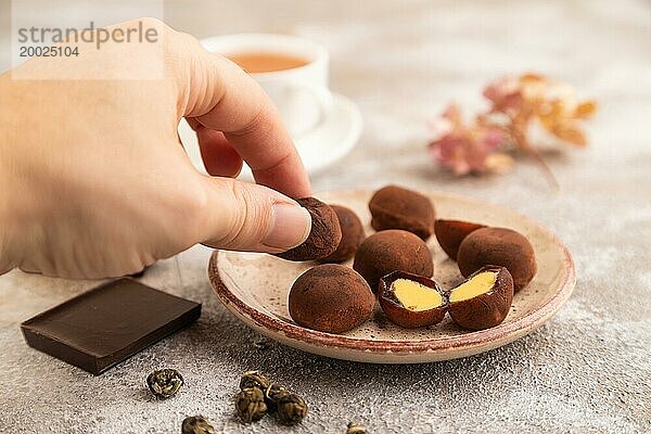 Japanischer Reis süße Brötchen Schokolade Mochi gefüllt mit Sahne und Tasse grüner Tee und Hand auf braunem Beton Hintergrund. Seitenansicht  Nahaufnahme  selektiver Fokus