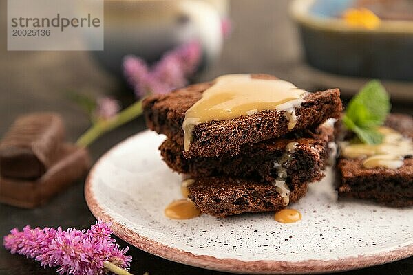 Schokolade Brownie mit Karamell Sauce mit einer Tasse Kaffee auf schwarzem Beton Hintergrund. Seitenansicht  Nahaufnahme  selektiver Fokus