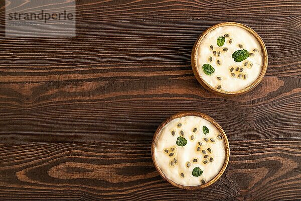 Joghurt mit Granadilla und Minze in Holzschüssel auf braunem Holzhintergrund. Draufsicht  flat lay  copy space